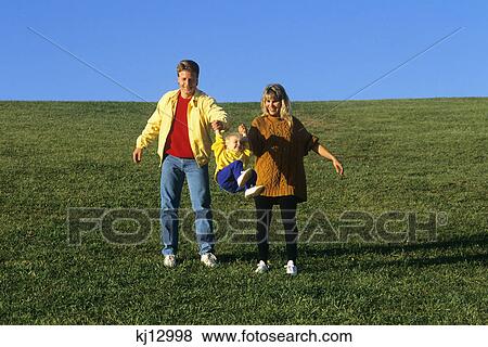 father and mother swinging daughter by the arms on grassy hill View Large Photo Image Stock Photo - father and mother swinging daughter by the arms on grassy hill. Fotosearch