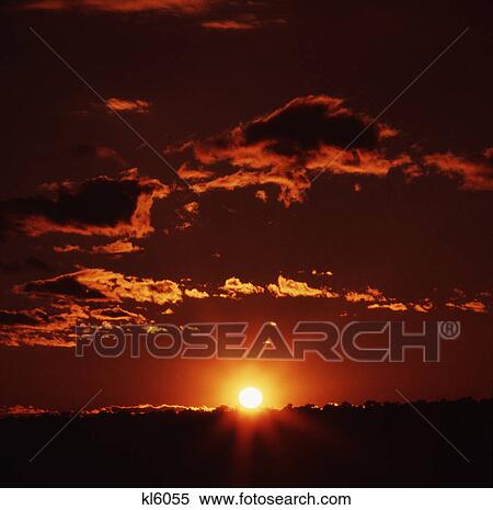 Stock Photography - landscape of yellow ball of sun setting on the horizon with red orange sky. Fotosearch