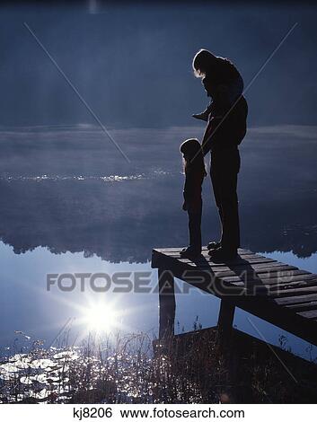 moody silhouette of man father and two daughters one on his shoulders other standing on dock looking at lake View Large Photo Image Stock Photograph - moody silhouette of man father and two daughters one on his shoulders other standing on dock looking at lake. Fotosearch