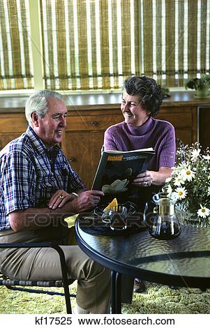 Stock Photography - senior couple seated at table with coffee reading magazine. Fotosearch