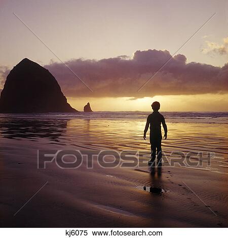 Stock Photography - silhouetted boy walking on beach at sunset haystack rock near cannon beach oregon. Fotosearch