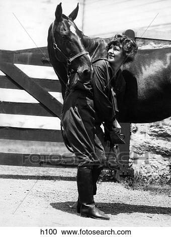 Stock Image - 1900S 1910S Young Woman With Upswept Hair Lifting Front Leg Of Horse Checking Cleaning Hoof. Fotosearch
