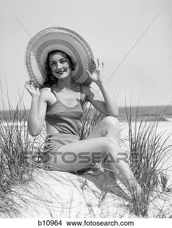 1920S 1930 Smiling Bathing Beauty Wearing Straw Hat Sitting On Beach Sand Dune Looking At Camera View Large Photo Image Picture - 1920S 1930 Smiling Bathing Beauty Wearing Straw Hat Sitting On Beach Sand Dune Looking At Camera. Fotosearch