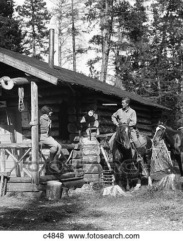 1920S 1930S Couple In Front Of Log Cabin Woman Sitting On Porch Railing Man On Horse Alberta Canada View Large Photo Image Stock Photo - 1920S 1930S Couple In Front Of Log Cabin Woman Sitting On Porch Railing Man On Horse Alberta Canada. Fotosearch