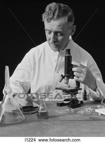1920S 1930S Male Scientist Wearing White Lab Coat Writing Data On Clip Board Holding Focus Control Of Microscope View Large Photo Image Picture - 1920S 1930S Male Scientist Wearing White Lab Coat Writing Data On Clip Board Holding Focus Control Of Microscope. Fotosearch