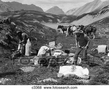 1920S 1930S Three Men Cowboys At Campsite Preparing Food Horses In Background Alberta Canada View Large Photo Image Stock Photo - 1920S 1930S Three Men Cowboys At Campsite Preparing Food Horses In Background Alberta Canada. Fotosearch