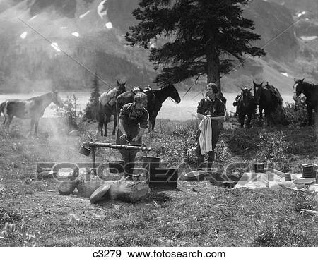 1920S 1930S Two Women At Campsite Woman Cooking Preparing Food Over Campfire Horses With Riding Gear In Background View Large Photo Image Stock Photo - 1920S 1930S Two Women At Campsite Woman Cooking Preparing Food Over Campfire Horses With Riding Gear In Background. Fotosearch