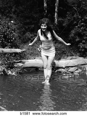 Stock Image - 1920S Long-Haired Woman In Old Fashion Bathing Suit Standing In Pond With Feet In Water About To Dive Outdoor. Fotosearch