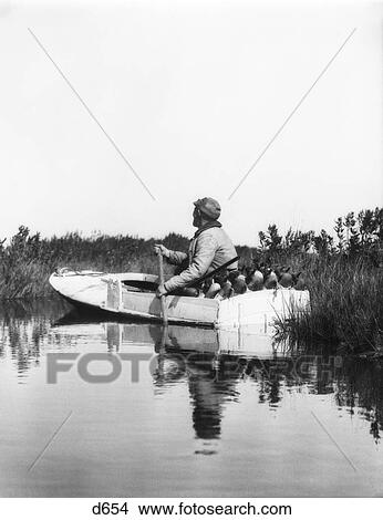 1920S Man Hunter Paddling Small Boat Through Wetlands Marsh Duck Decoys And Shotgun In Back Of Boat View Large Photo Image Picture - 1920S Man Hunter Paddling Small Boat Through Wetlands Marsh Duck Decoys And Shotgun In Back Of Boat. Fotosearch
