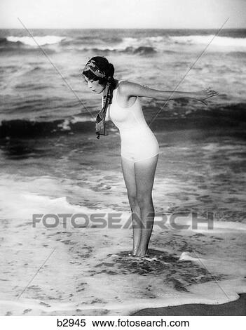 1920S Woman Wearing Bathing Suit & Head Scarf Looking Down At Water Standing In Ocean Surf View Large Photo Image Stock Photography - 1920S Woman Wearing Bathing Suit & Head Scarf Looking Down At Water Standing In Ocean Surf . Fotosearch