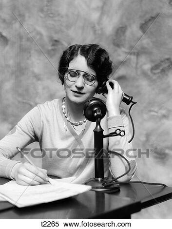 1920S Woman Wearing Pince-Nez Glasses Sitting At Desk Talking On Candlestick Phone And Writing View Large Photo Image Stock Photography - 1920S Woman Wearing Pince-Nez Glasses Sitting At Desk Talking On Candlestick Phone And Writing. Fotosearch