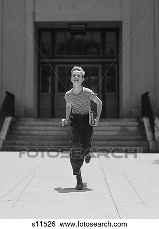 Stock Photograph - 1930S 1940S Boy Running From School Carrying Books Looking At Camera. Fotosearch