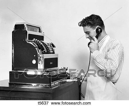 1930S 1940S Man In Apron Next To Large Cash Register Talking On Phone Taking Notes Smiling View Large Photo Image Stock Photo - 1930S 1940S Man In Apron Next To Large Cash Register Talking On Phone Taking Notes Smiling. Fotosearch