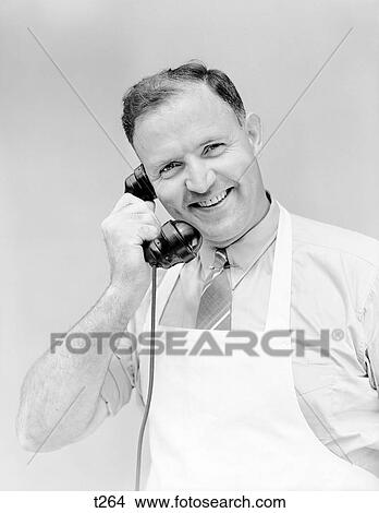 1930S 1940S Man Wearing White Apron Smiling Talking On Telephone Store Clerk Butcher Baker Grocer Service Business Looking At Camera View Large Photo Image Picture - 1930S 1940S Man Wearing White Apron Smiling Talking On Telephone Store Clerk Butcher Baker Grocer Service Business Looking At Camera. Fotosearch