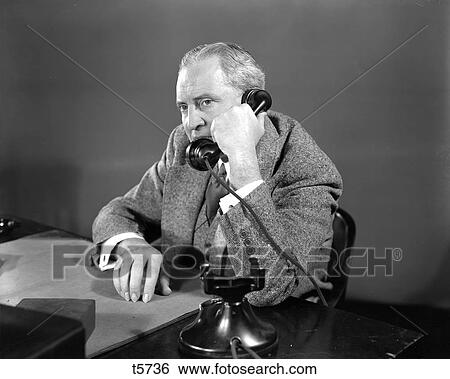 1930S 1940S Suspicious Businessman Talking On Telephone Sitting At Desk View Large Photo Image Stock Photograph - 1930S 1940S Suspicious Businessman Talking On Telephone Sitting At Desk. Fotosearch