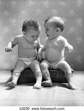 Stock Image - 1930S 1940S Twin Babies Wearing Diapers Together Sitting On A Bench Side By Side Studio. Fotosearch