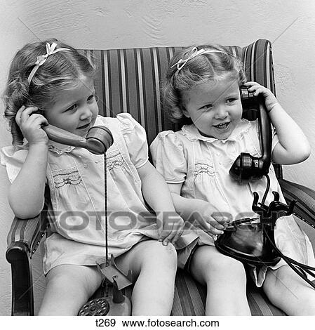 1930S 1940S Twin Little Girls Sisters Together Talking On Real And Toy Telephones Smiling Sitting Together In Chair View Large Photo Image Stock Photo - 1930S 1940S Twin Little Girls Sisters Together Talking On Real And Toy Telephones Smiling Sitting Together In Chair. Fotosearch