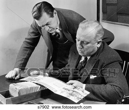 1930S 1940S Two Salesmen Looking At Sales Brochure Sitting At A Desk With Client Card File View Large Photo Image Stock Image - 1930S 1940S Two Salesmen Looking At Sales Brochure Sitting At A Desk With Client Card File. Fotosearch