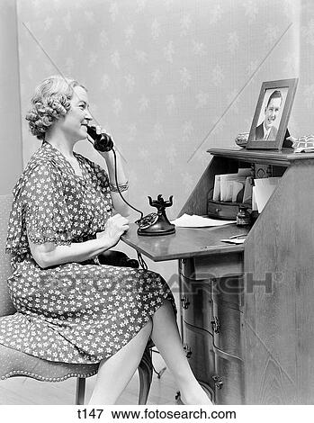1930S 1940S Woman Mother Talking On Telephone Looking At Picture Of Absent Son Parent Love Communication Pride View Large Photo Image Stock Photo - 1930S 1940S Woman Mother Talking On Telephone Looking At Picture Of Absent Son Parent Love Communication Pride . Fotosearch