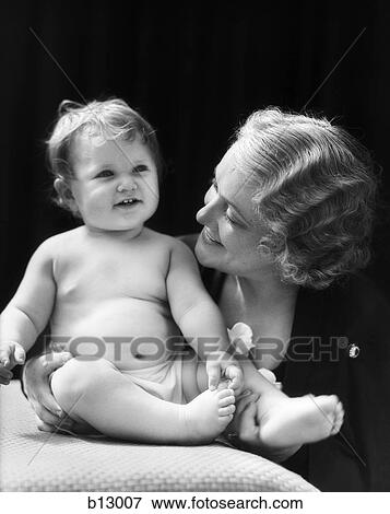 Stock Photo - 1930S Blond Woman Mother Smiling Looking At Baby Sitting On Pillow. Fotosearch