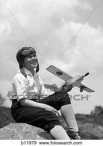 1930S Boy In Leather Aviator Cap With Goggles Sitting On Rock Holding Model Plane View Large Photo Image Stock Photo - 1930S Boy In Leather Aviator Cap With Goggles Sitting On Rock Holding Model Plane. Fotosearch