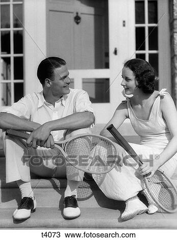 1930S Couple Man Woman In Tennis Whites Holding Racquets Sitting Talking On Steps In Front Of House Outdoor View Large Photo Image Stock Image - 1930S Couple Man Woman In Tennis Whites Holding Racquets Sitting Talking On Steps In Front Of House Outdoor. Fotosearch
