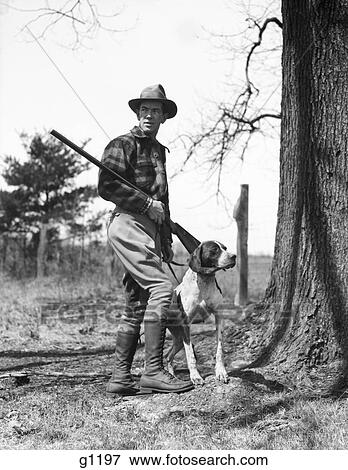 1930S Man Hunter Wearing Hat Plaid Flannel Shirt Jodhpurs And Boots Standing Holding Shotgun With Pointer Dog View Large Photo Image Stock Photo - 1930S Man Hunter Wearing Hat Plaid Flannel Shirt Jodhpurs And Boots Standing Holding Shotgun With Pointer Dog. Fotosearch
