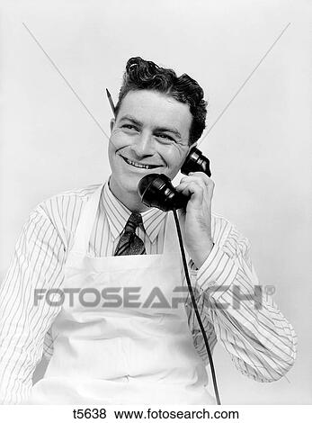1930S Portrait Smiling Man Wearing Apron Talking On Telephone Pencil Behind Ear Butcher Baker Grocery Clerk Service Curly Hair View Large Photo Image Stock Photo - 1930S Portrait Smiling Man Wearing Apron Talking On Telephone Pencil Behind Ear Butcher Baker Grocery Clerk Service Curly Hair. Fotosearch