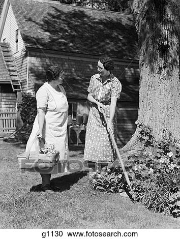 1930S Two Women Talking In Yard One Holding Garden Hoe The Other Holds Basket With Flowers View Large Photo Image Stock Image - 1930S Two Women Talking In Yard One Holding Garden Hoe The Other Holds Basket With Flowers . Fotosearch