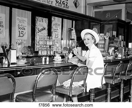 1930S Woman In White Dress & Hat Sitting At Soda Fountain Counter Eating Ice Cream Sundae View Large Photo Image Stock Photograph - 1930S Woman In White Dress & Hat Sitting At Soda Fountain Counter Eating Ice Cream Sundae. Fotosearch