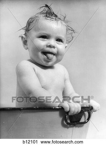 Stock Image - 1940S 1930S Wet Baby Sitting In Tub Sticking Out Tongue. Fotosearch
