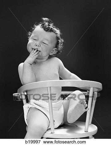 1940S 1950S Baby Sitting Backwards In High Chair With One Leg In Air Eyes Closed & Hand On Mouth View Large Photo Image Stock Photo - 1940S 1950S Baby Sitting Backwards In High Chair With One Leg In Air Eyes Closed & Hand On Mouth. Fotosearch