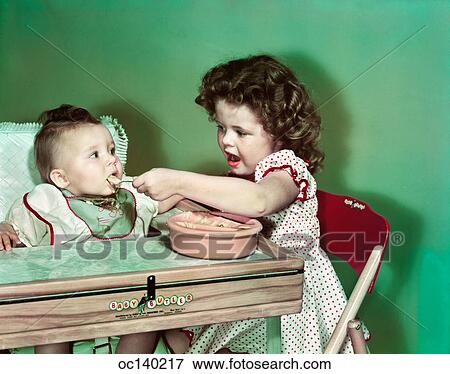 1940S 1950S Girl Sitting Feeding Baby Sister In High Chair View Large Photo Image Stock Photo - 1940S 1950S Girl Sitting Feeding Baby Sister In High Chair. Fotosearch