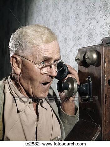 Stock Image - 1940S 1950S Man Using Old-Fashioned Wall Mounted Telephone. Fotosearch