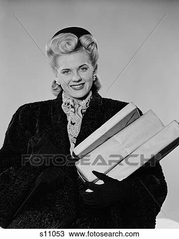 Stock Image - 1940S Blond Woman Smiling Wearing Winter Coat Carrying Shopping Parcel Looking At Camera. Fotosearch