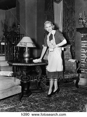 1940S Blonde Woman Housewife Maid Wearing Apron Cleaning Polishing Wooden End Table In Ornate Living Room View Large Photo Image Stock Image - 1940S Blonde Woman Housewife Maid Wearing Apron Cleaning Polishing Wooden End Table In Ornate Living Room. Fotosearch