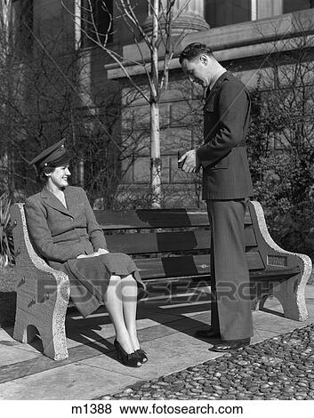 Stock Photo - 1940S Couple Man In Army Uniform Taking Photo Of Woman Sitting On Bench Wearing Hat. Fotosearch