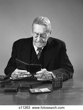 1940S Elderly Man Wearing Glasses Sitting At Table Looking At Daguerreotype Photographs View Large Photo Image Stock Image - 1940S Elderly Man Wearing Glasses Sitting At Table Looking At Daguerreotype Photographs. Fotosearch