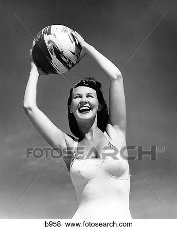 1940S Smiling Woman In White Bathing Suit Holding A Beach Ball Over Her Head Outdoor View Large Photo Image Stock Photo - 1940S Smiling Woman In White Bathing Suit Holding A Beach Ball Over Her Head Outdoor. Fotosearch