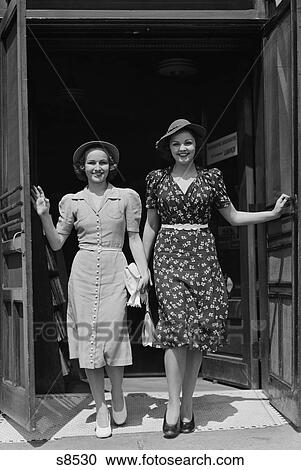 Stock Image - 1940S Two Smiling Women Walking Out Doorway Of A Store. Fotosearch