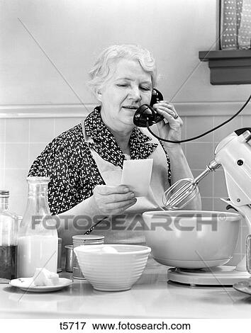 1940S Woman Grandmother Housewife Cook In Kitchen Wearing Apron With Food Mixer Reading Ingredients List Talking On Telephone View Large Photo Image Stock Photo - 1940S Woman Grandmother Housewife Cook In Kitchen Wearing Apron With Food Mixer Reading Ingredients List Talking On Telephone. Fotosearch