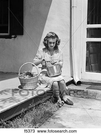 1940S Woman Wearing Plaid Dress And Apron Sitting On Porch Of Farmhouse With Basket Of Vegetables Peeling Tomato Over Pot View Large Photo Image Stock Image - 1940S Woman Wearing Plaid Dress And Apron Sitting On Porch Of Farmhouse With Basket Of Vegetables Peeling Tomato Over Pot. Fotosearch