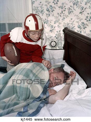 1950S 1960S Boy In Football Uniform Waking Father Asleep In Bedroom View Large Photo Image Stock Photography - 1950S 1960S Boy In Football Uniform Waking Father Asleep In Bedroom . Fotosearch