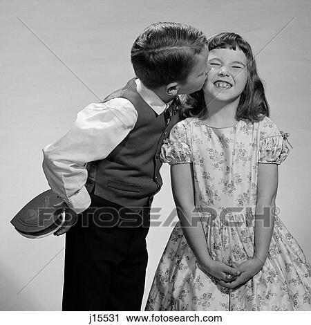 Stock Image - 1950S 1960S Boy In Vest & Bow Tie Holding Valentine Candy Kissing Cheek Of Girl Making A Face. Fotosearch