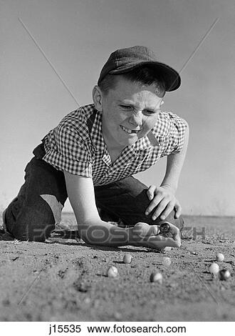 1950S 1960S Boy Playing Marbles Kneeling In The Dirt Squinting Missing A Front Tooth View Large Photo Image Stock Photography - 1950S 1960S Boy Playing Marbles Kneeling In The Dirt Squinting Missing A Front Tooth. Fotosearch