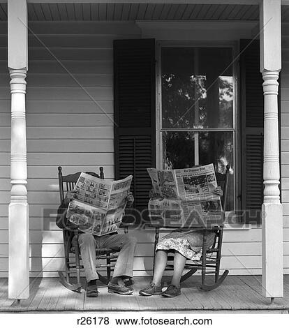 Stock Photo - 1950S 1960S Couple Man Woman Sitting On Porch In Rocking Chairs Holding Newspapers Up Hiding Their Faces. Fotosearch