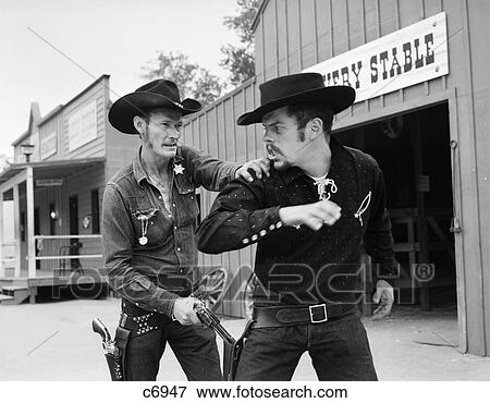 Stock Photo - 1950S 1960S Cowboy Sheriff Marshall Nabs Arrest Gunfighter Outlaw Near Livery Stable. Fotosearch