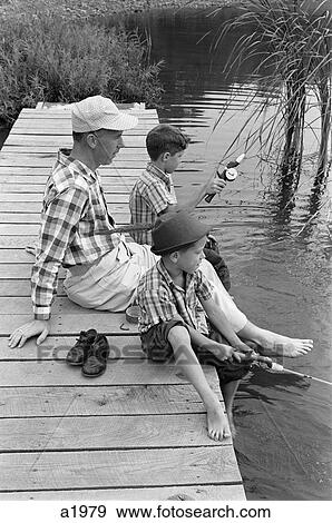 Stock Photo - 1950S 1960S Father With Two Sons Sitting On Dock Fishing Together Outdoor By Pond. Fotosearch