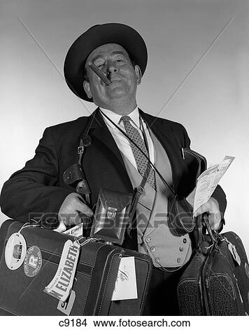 Picture - 1950S 1960S Head-On Portrait Of Cigar Smoking Tourist Carrying Lots Of Luggage Looking At Camera. Fotosearch