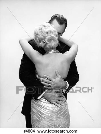 Picture - 1950S 1960S Kissing Couple Blond Woman Backless Satin Evening Dress Man Embracing From Behind . Fotosearch